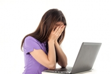 A woman sitting in front of a computer covers her face with her hands. She looks embarrassed. 