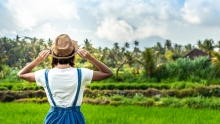 Woman in fedora faces away from camera and looks out on a scene of grass and trees